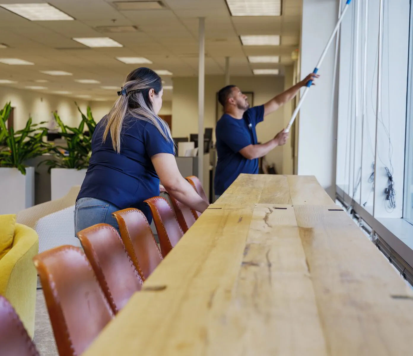 Two ExtraClean team members dusting high along a long office window counter
