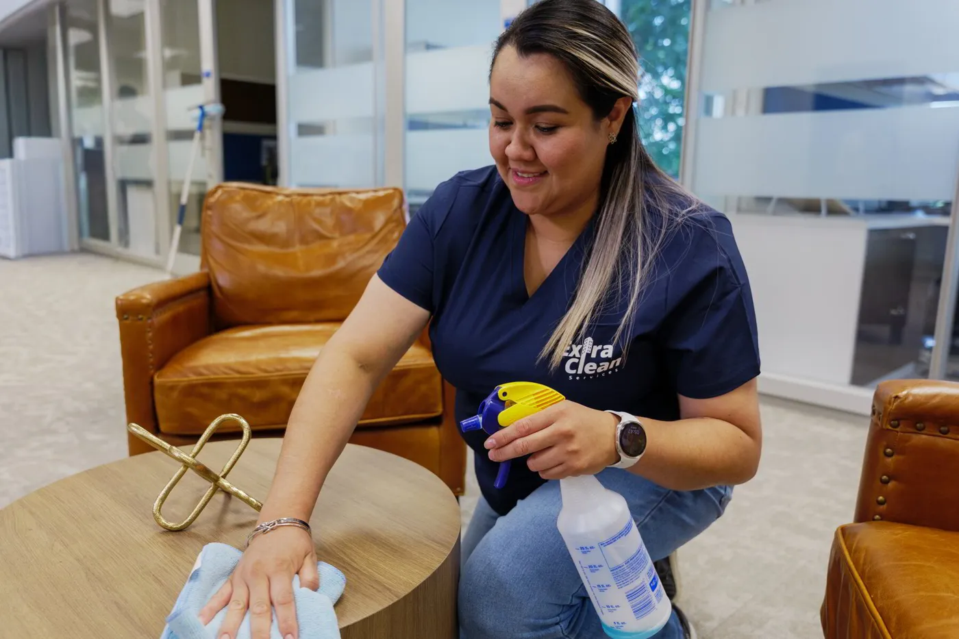 An ExtraClean team member wiping a round wooden table in an office lounge